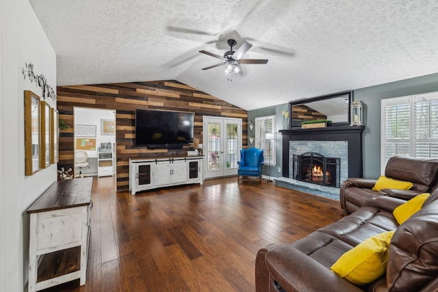 living room featuring wooden walls, hardwood / wood-style flooring, a ceiling fan, a lit fireplace, and vaulted ceiling