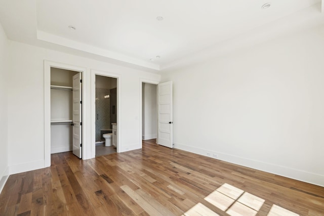 unfurnished bedroom featuring baseboards, a closet, wood finished floors, and a walk in closet