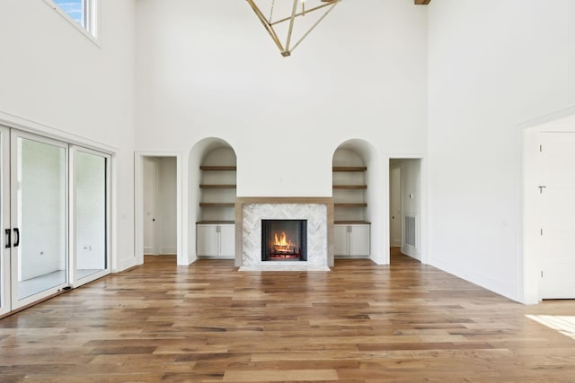unfurnished living room with built in shelves, a premium fireplace, light wood-type flooring, baseboards, and visible vents
