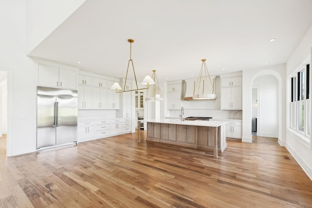 kitchen with light countertops, a sink, arched walkways, built in fridge, and light wood-style floors