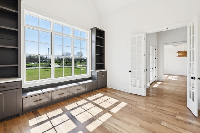 interior space with baseboards, light wood-style flooring, a towering ceiling, and french doors