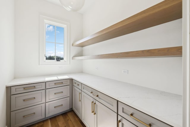 interior space featuring dark wood-type flooring, gray cabinets, light stone counters, and open shelves