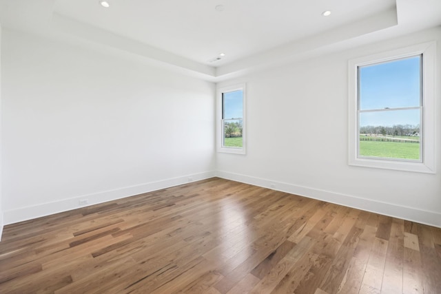 unfurnished room with a tray ceiling, baseboards, recessed lighting, and hardwood / wood-style flooring