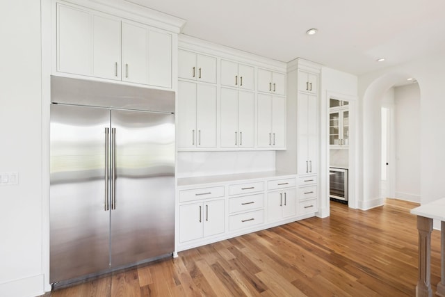 kitchen with light wood finished floors, arched walkways, white cabinetry, beverage cooler, and built in refrigerator