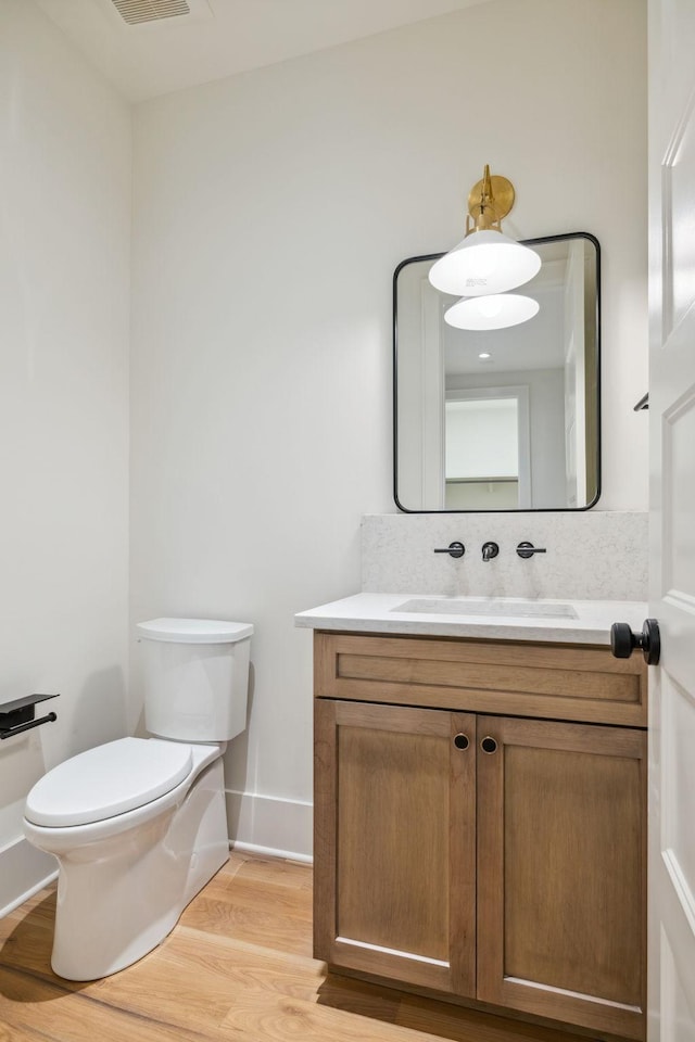 half bath with baseboards, toilet, vanity, and wood finished floors