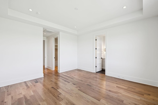 unfurnished room with visible vents, a tray ceiling, baseboards, and wood finished floors