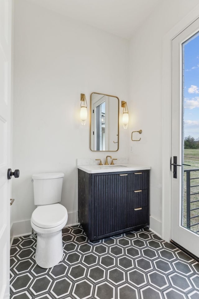 half bath with baseboards, toilet, vanity, and tile patterned floors