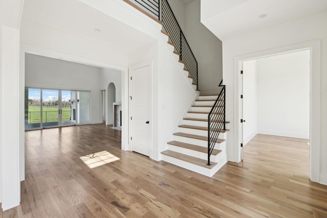 stairway with baseboards, wood finished floors, arched walkways, and a towering ceiling
