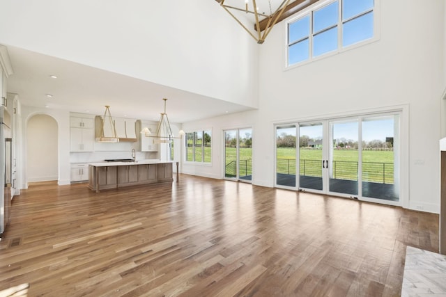 unfurnished living room with light wood-style flooring, baseboards, arched walkways, and an inviting chandelier