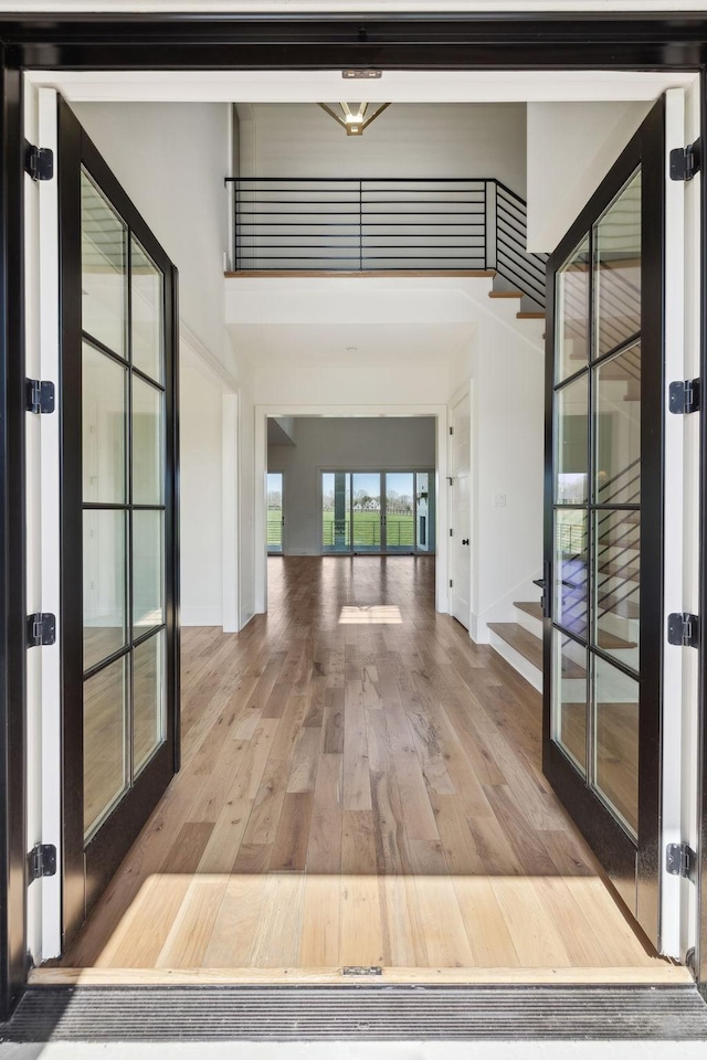 hallway featuring baseboards, stairs, a high ceiling, french doors, and wood-type flooring