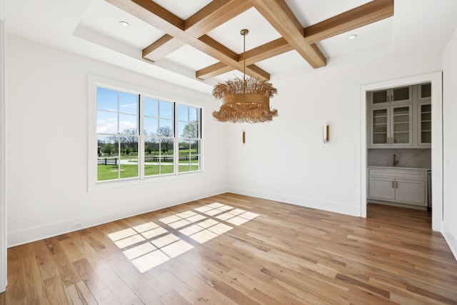 empty room featuring baseboards, an inviting chandelier, coffered ceiling, and light wood finished floors