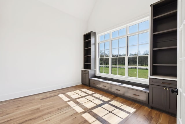 empty room featuring baseboards, high vaulted ceiling, and light wood-style flooring