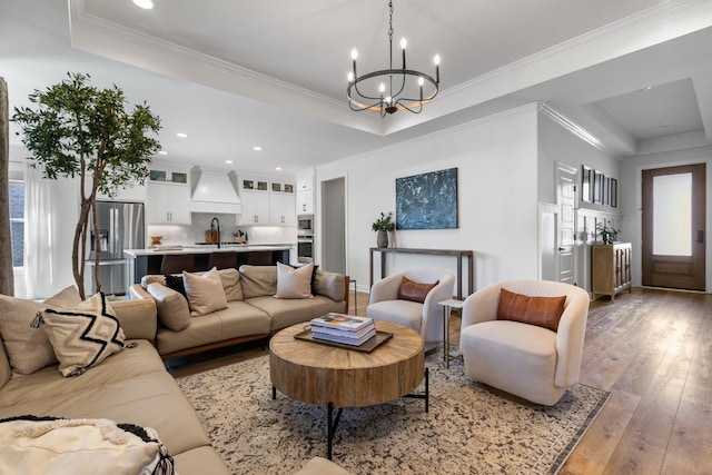 living room with a tray ceiling, a notable chandelier, light wood-style flooring, ornamental molding, and recessed lighting