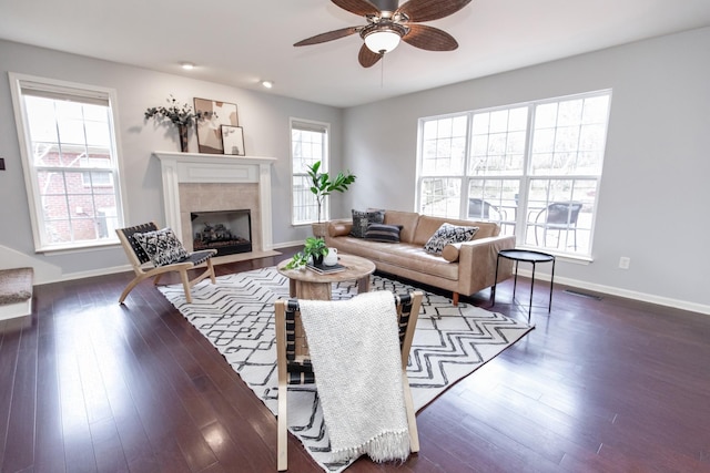 living area featuring visible vents, a ceiling fan, a tiled fireplace, and dark wood-style flooring