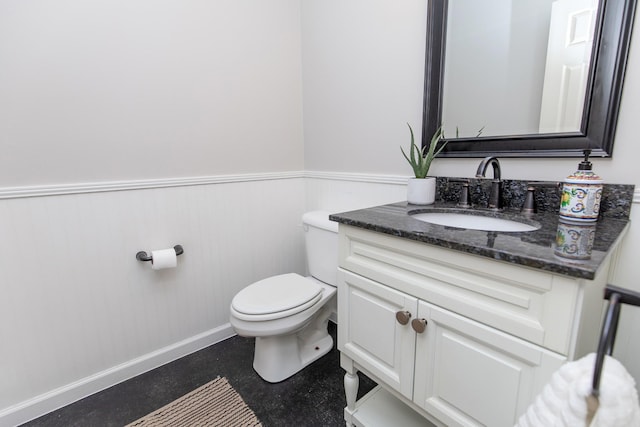 half bathroom with concrete floors, wainscoting, toilet, and vanity