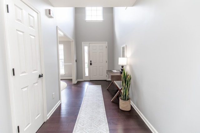 entryway featuring a towering ceiling, dark wood-style floors, and baseboards