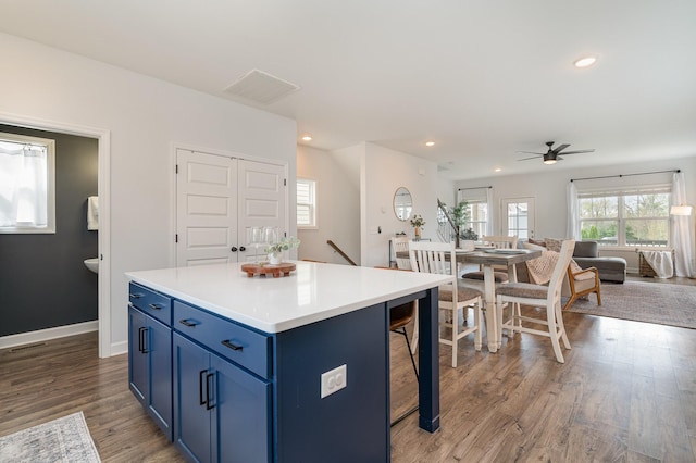 kitchen featuring ceiling fan, light wood-type flooring, blue cabinetry, a kitchen island, and open floor plan