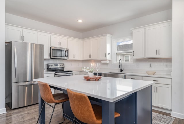 kitchen with backsplash, a kitchen island, white cabinets, appliances with stainless steel finishes, and a sink