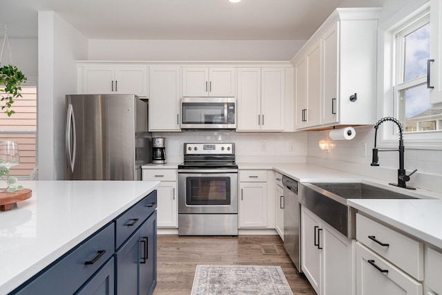 kitchen with light countertops, white cabinets, stainless steel appliances, a sink, and wood finished floors