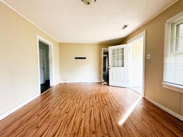 empty room with baseboards, wood finished floors, a textured ceiling, and a healthy amount of sunlight