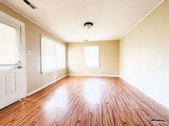 empty room featuring wood finished floors, a textured ceiling, baseboards, and visible vents