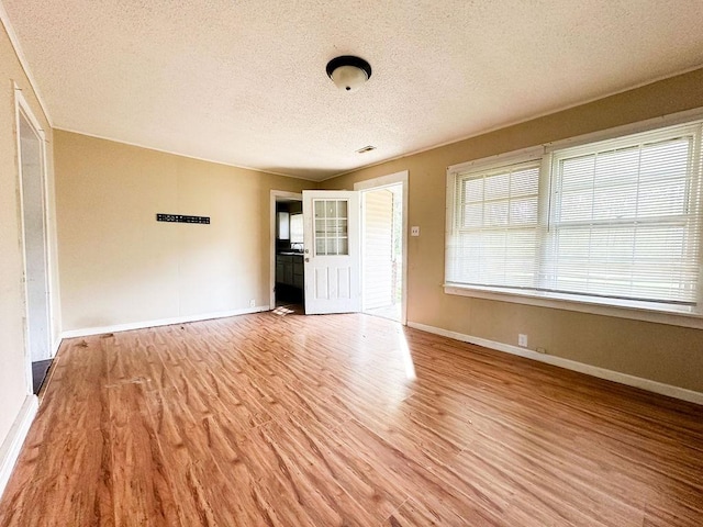 spare room with a textured ceiling, light wood finished floors, and baseboards