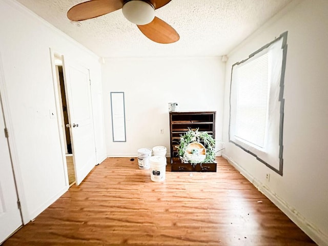 unfurnished living room with wood finished floors, a textured ceiling, a ceiling fan, and baseboards