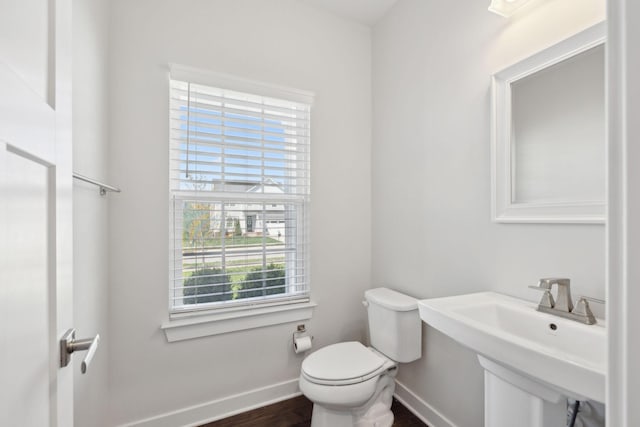 half bath with baseboards, a sink, toilet, and a healthy amount of sunlight