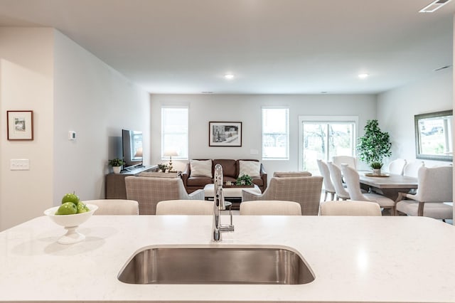 kitchen featuring open floor plan, a center island with sink, a sink, visible vents, and light stone countertops