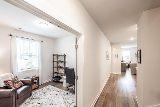 hall featuring visible vents, baseboards, and wood finished floors