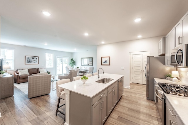 kitchen featuring gray cabinets, a sink, a breakfast bar, stainless steel appliances, and a kitchen island with sink