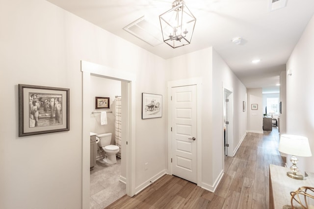 corridor with baseboards, a notable chandelier, visible vents, and light wood-style flooring