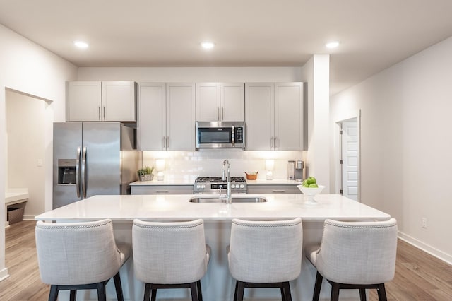 kitchen with decorative backsplash, a breakfast bar, stainless steel appliances, a sink, and light wood-type flooring