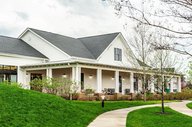 view of front of property with a porch, roof with shingles, and a front lawn