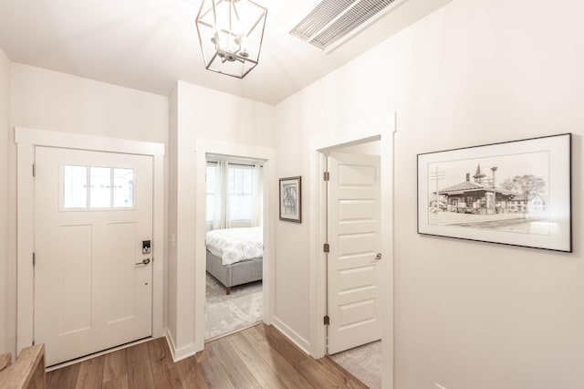 foyer entrance with light wood-type flooring, a notable chandelier, baseboards, and visible vents