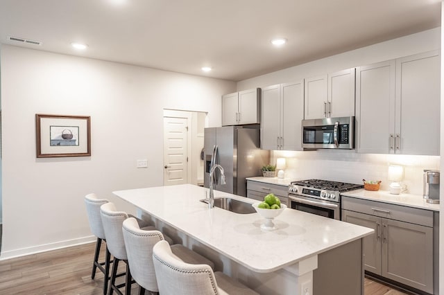 kitchen with a sink, a kitchen bar, gray cabinetry, stainless steel appliances, and visible vents