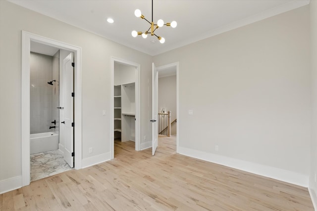 unfurnished bedroom with a spacious closet, light wood-style flooring, a notable chandelier, and baseboards