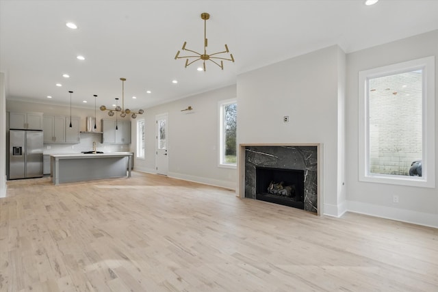 unfurnished living room featuring a notable chandelier, a high end fireplace, light wood-style flooring, and recessed lighting