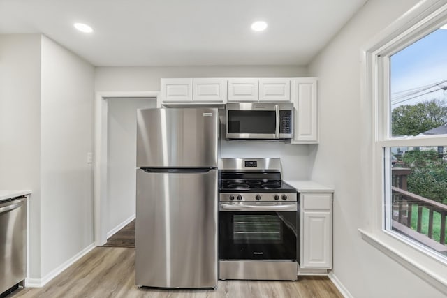 kitchen with stainless steel appliances, light wood-style flooring, light countertops, white cabinets, and baseboards