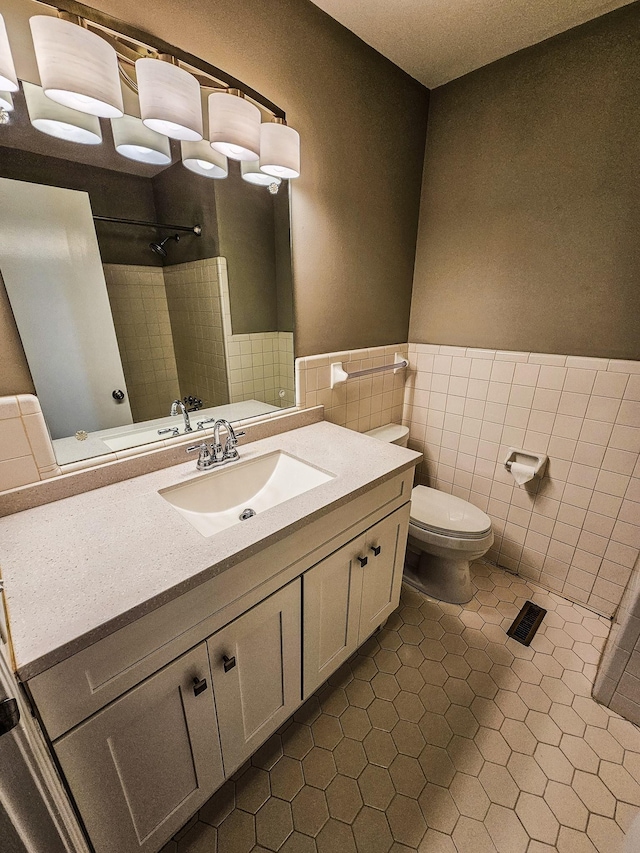 bathroom featuring a wainscoted wall, toilet, vanity, walk in shower, and tile walls