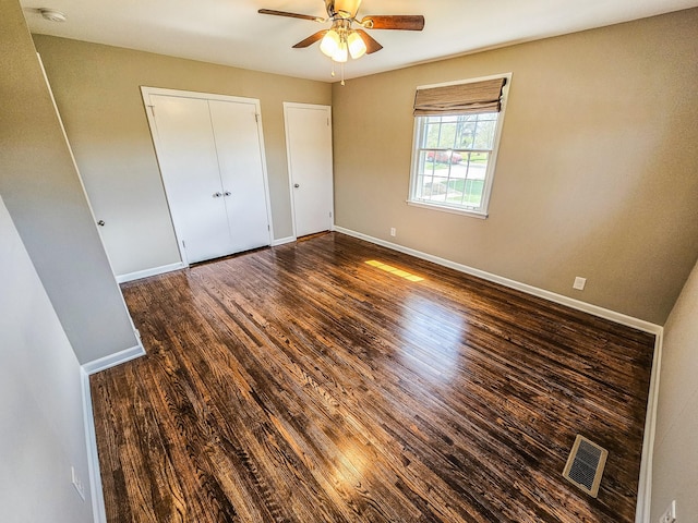 unfurnished bedroom featuring baseboards, two closets, visible vents, and wood finished floors