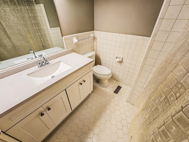 full bath featuring tile patterned flooring, vanity, tile walls, toilet, and wainscoting