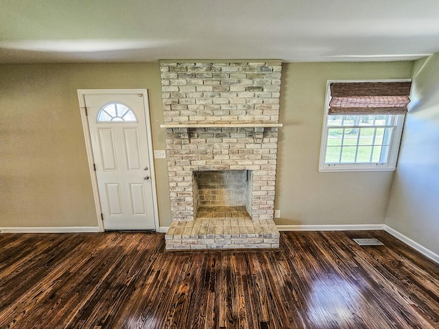 unfurnished living room with baseboards, visible vents, wood finished floors, and a brick fireplace