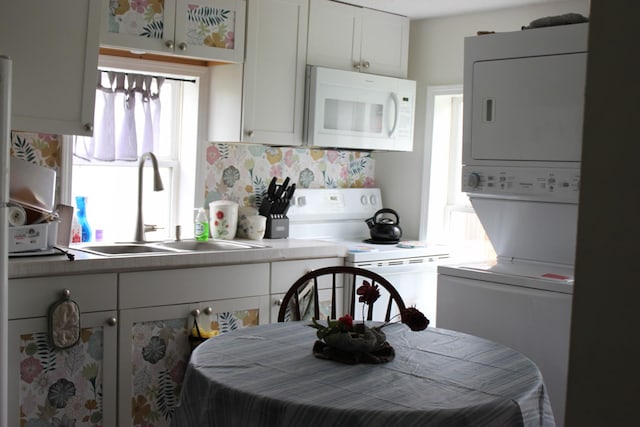 kitchen with white appliances, decorative backsplash, stacked washer and dryer, a sink, and white cabinets