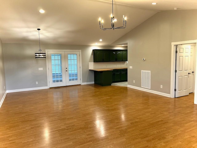 unfurnished living room featuring lofted ceiling, baseboards, visible vents, a notable chandelier, and wood finished floors