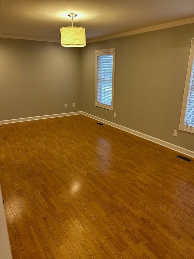 spare room featuring visible vents, crown molding, baseboards, and dark wood-type flooring