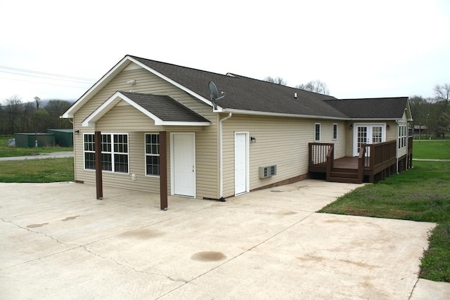 rear view of property with a shingled roof, a lawn, a wooden deck, and a patio area
