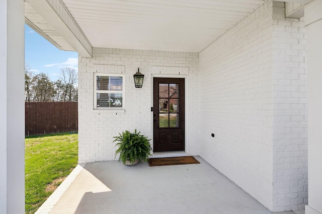 view of exterior entry featuring a lawn, brick siding, and fence