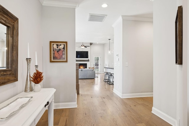 hall with light wood-style flooring, crown molding, baseboards, and visible vents