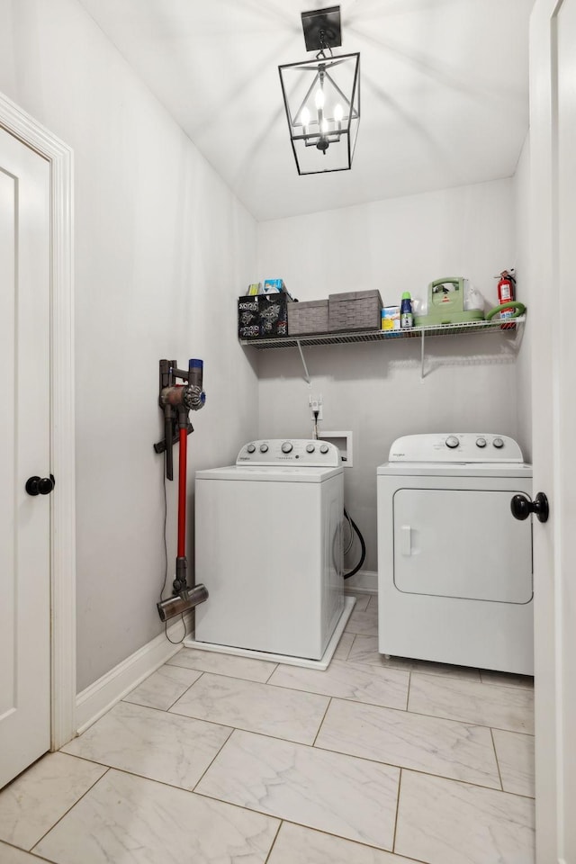 clothes washing area with washing machine and dryer, laundry area, marble finish floor, baseboards, and an inviting chandelier